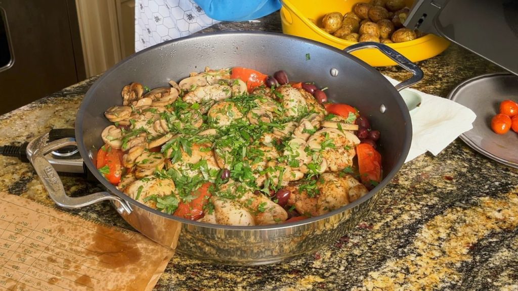 An image of chicken marengo cooked inside of an electric skillet. The chicken marengo is topped with parsley. The dish contains chicken, tomatoes, and olives.
